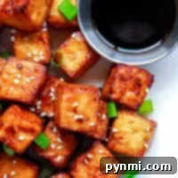 Golden brown tofu cubes, perfectly crisped in the air fryer, sprinkled with sesame seeds and green onions, served with a small dish of dark soy sauce.