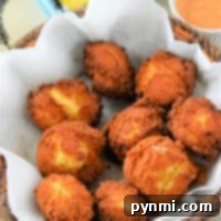 A basket of crispy, Jiffy Mix hush puppies with a tangy dipping sauce, all cozily nestled in parchment paper.