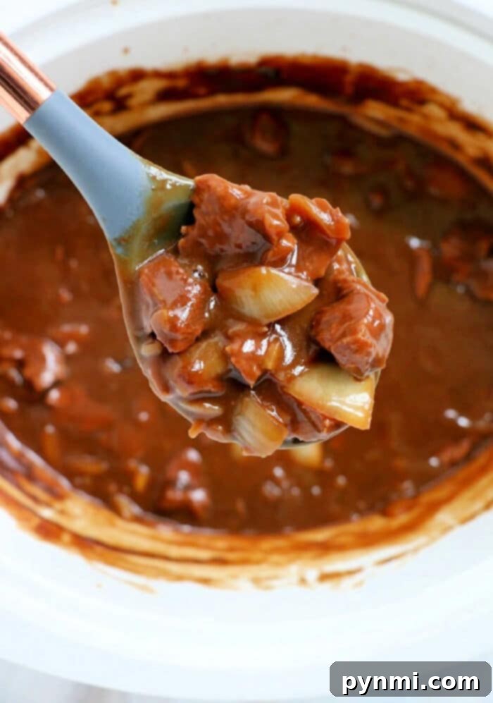 A spoonful of hearty beef tips above a slow cooker brimming with tender beef tips and more delicious stew.