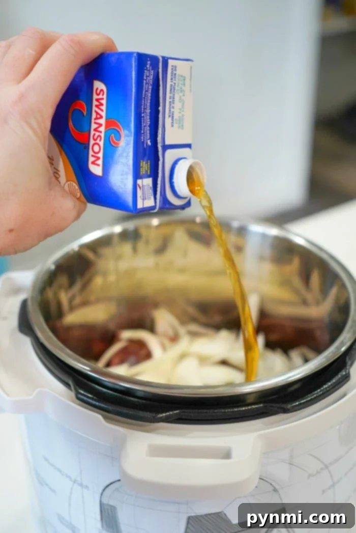 Pouring broth from a carton into a pressure cooker with sliced onions inside, preparing the base for a savory Instant Pot BBQ beef dish.
