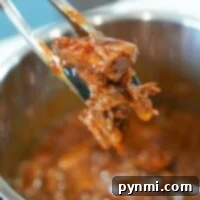 Tongs holding flavorful, shredded Instant Pot BBQ beef above a pot of simmering sauce.