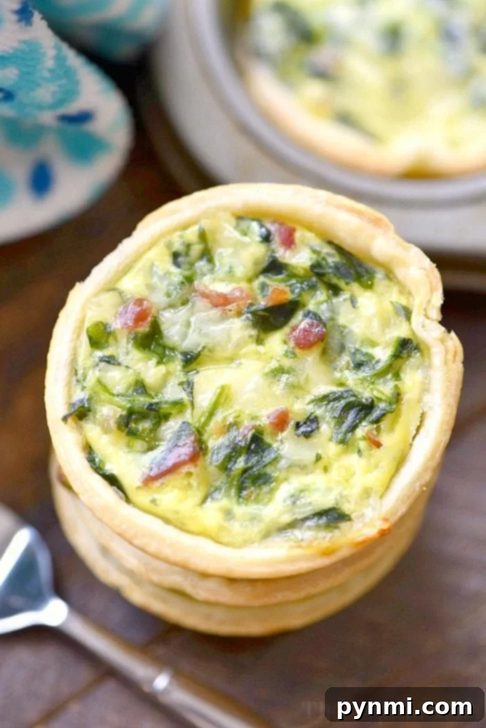 Close-up of a mini spinach and bacon quiche on a wooden table, with a fork next to it, inviting a taste.
