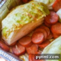 Smoked sausage and cabbage slices arranged in a foil pan, seasoned and ready for the smoker
