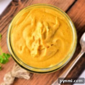 A jar of creamy yellow mustard sauce for corned beef sits on a wooden board, accompanied by a spoon and a twine decoration nearby.