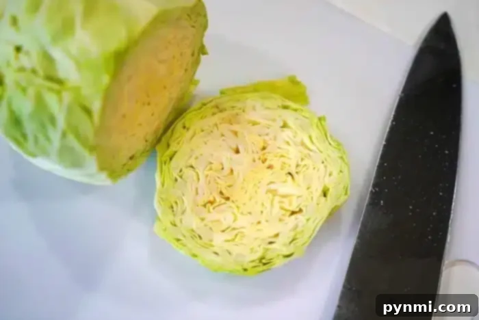 Hearty Cabbage Steaks 3 A halved cabbage is placed on a white surface next to a large kitchen knife, ready to be transformed into delicious baked cabbage steaks. The inner layers of the cabbage are visible, showcasing its tightly packed, light green and white leaves.