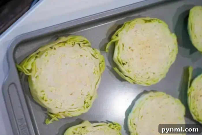 Hearty Cabbage Steaks 5 Slices of cabbage arranged on a baking sheet, ready for roasting or baking into delicious baked cabbage steaks. The cabbage is cut into thick rounds, showing the layers of leaves within each slice. The baking sheet is placed on a countertop.