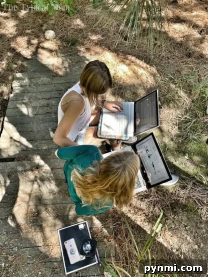 Complimentary K-12 Home Learning Solutions 2 Two people sit outdoors on a wooden pathway surrounded by foliage, utilizing laptops for free homeschool programs. The person on the left sports a white top, while the person on the right wears green. A smartphone rests on the ground nearby.