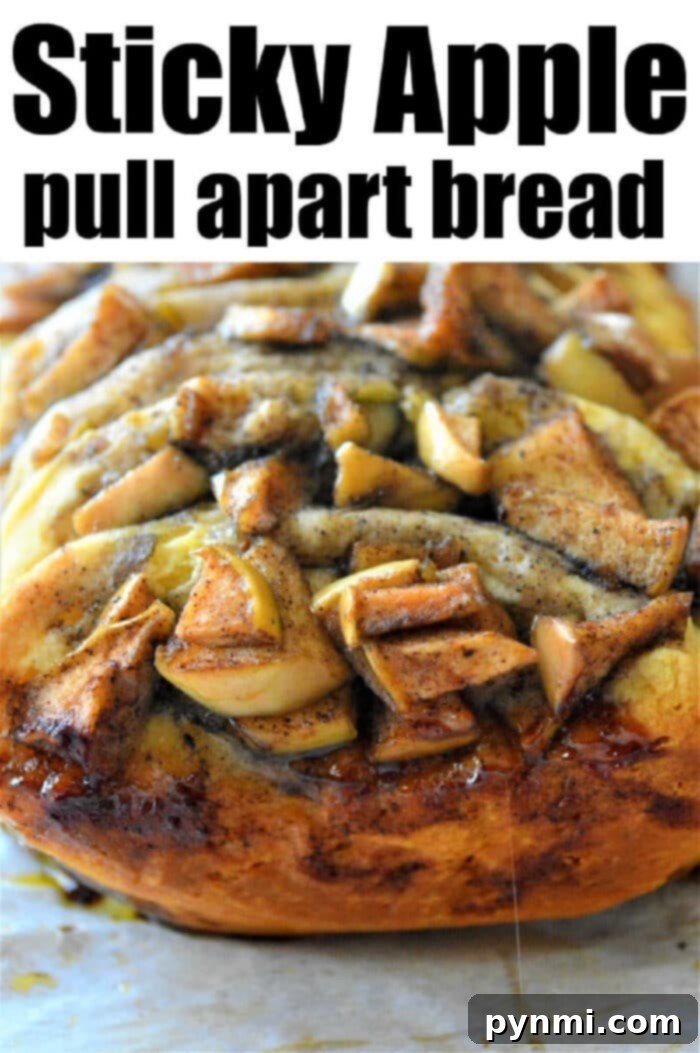 A loaf of sticky cinnamon pull apart bread is topped with baked apples and cinnamon, served warm on parchment paper, ready to be enjoyed.