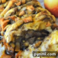 A close-up of a baked cinnamon pull-apart bread rests on parchment paper, with a fresh apple beside it, highlighting the warm and inviting aroma.