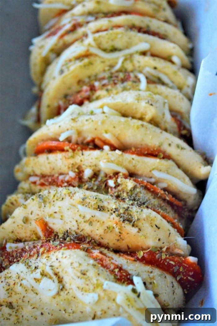 Ultimate Pizza Monkey Bread 4 Layers of pizza bread with refrigerated biscuits, cheese, and pepperoni in a loaf pan, ready for the oven
