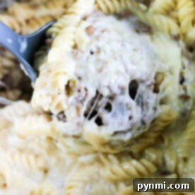 Close-up of creamy, cheesy rotini pasta with ground meat, reminiscent of a savory instant pot cheesesteak dish, being scooped with a serving spoon.