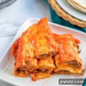 A plate of cheesy beef enchiladas, made perfectly in an instant pot, is artfully stacked on a white square plate with a hint of tortillas in the background.