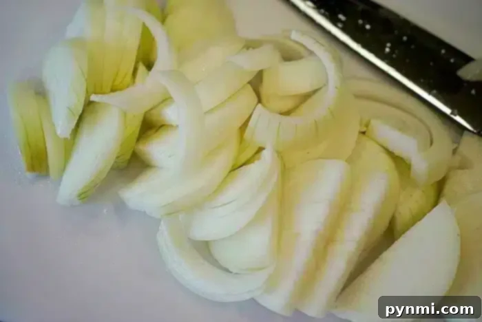 Crispy Air-Fried Onions 5 Slices of white onion on a cutting board next to a knife, ready to be transformed into crispy air fryer onions.