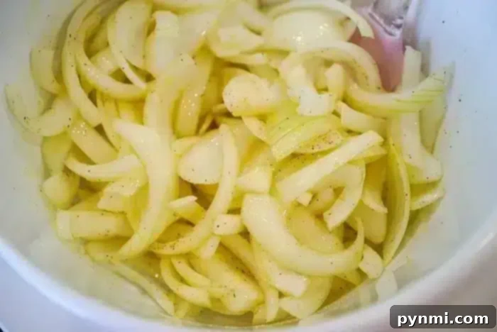 Crispy Air-Fried Onions 7 A close-up image of sliced onions in a white bowl, seasoned with a light sprinkling of salt and pepper after being perfectly crisped in the air fryer.