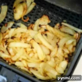 Crispy Air-Fried Onions 8 Sliced onions are being expertly cooked and slightly browned in the air fryer basket, transforming into deliciously crispy air fryer onions.