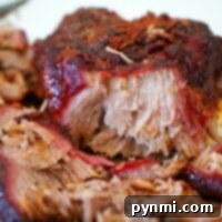 Pitmaster's Pulled Pork 9 Close-up of juicy, shredded smoked pulled pork with a crispy, caramelized exterior on a white plate, expertly prepared on a Traeger grill.