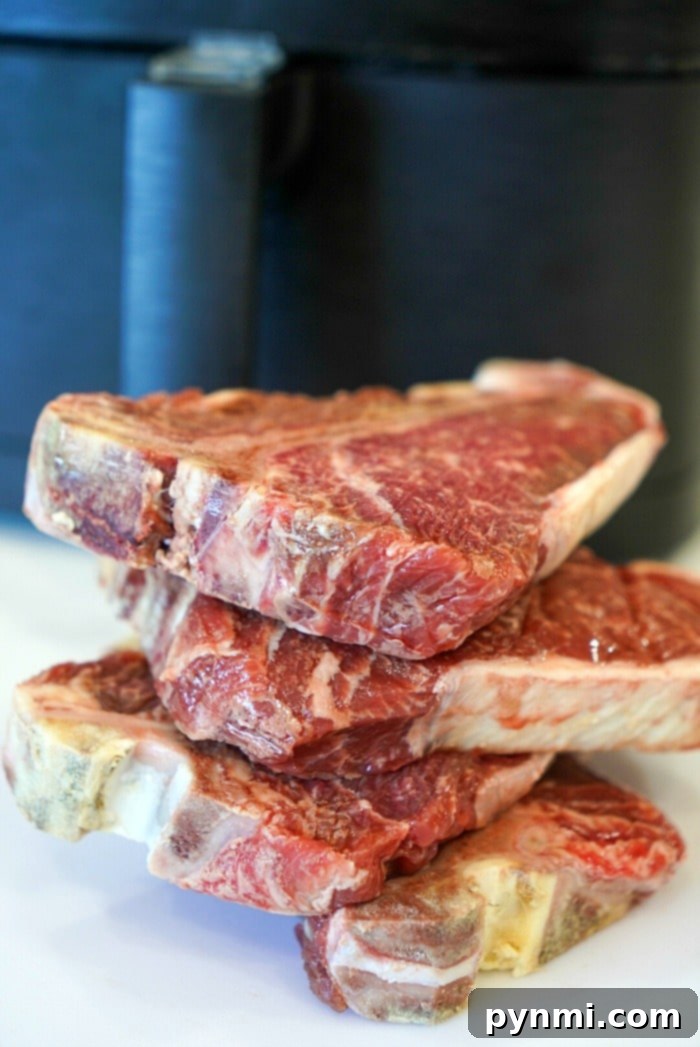 Juicy Air Fryer Steak Bites in Minutes 3 A pile of raw steaks, perfect for transforming into tender air fryer steak bites, is stacked on a counter against a dark background, ready for cooking bliss.