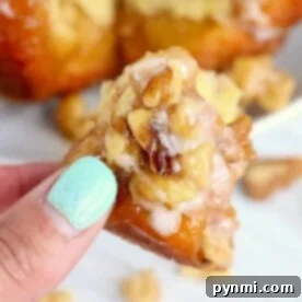 Close-up of a hand holding a piece of sticky nut pastry, reminiscent of air fryer monkey bread, with walnuts and icing.