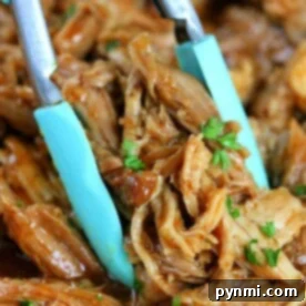 Close-up of a pair of tongs holding Ninja Foodi pulled pork, garnished with chopped herbs.