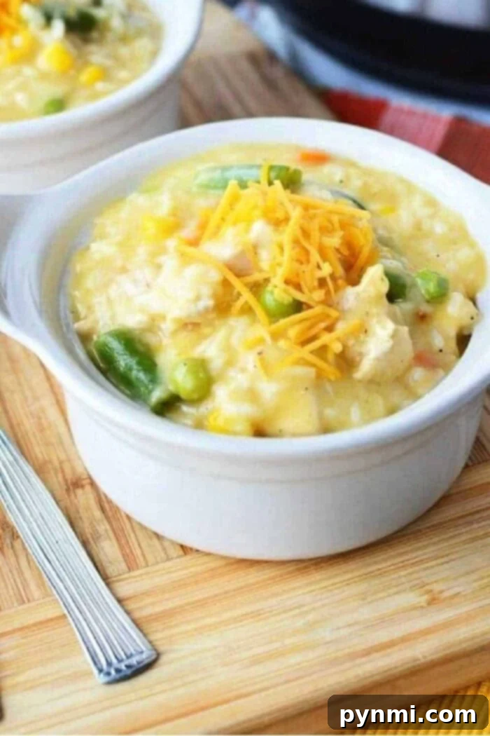 A bowl of creamy chicken and rice topped with shredded cheese on a wooden board, reminiscent of a comforting crockpot chicken casserole, sits invitingly beside a fork.