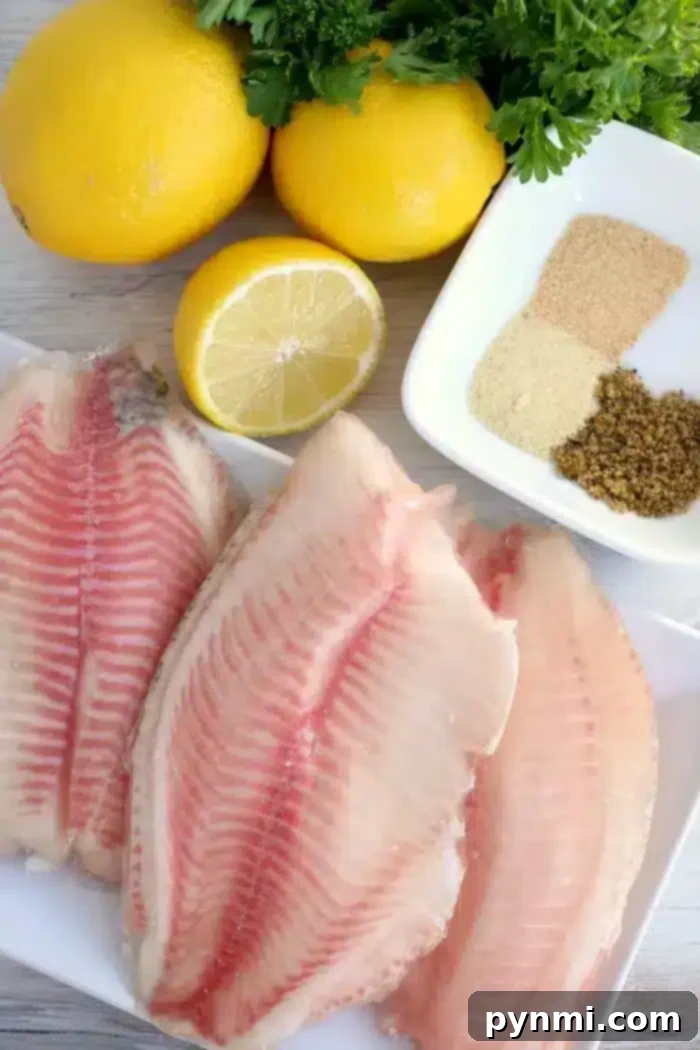 Three raw fish fillets are placed on a white plate, perfect for preparing air fryer fish. Beside the fillets are three whole lemons, one half lemon, a pile of fresh parsley, and a small dish containing brown and white spices. The image is set on a light-colored wooden surface.