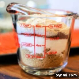 A clear measuring cup filled with salt and brown sugar sits on a wooden surface, resembling the perfect blend for a salmon dry rub.