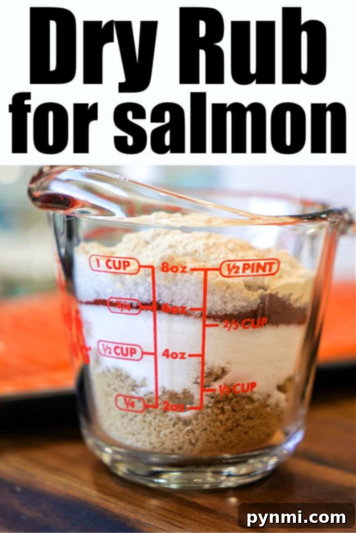 A measuring cup displaying perfectly mixed salmon dry rub, alongside individual spice ingredients on a wooden board, highlighting the simple components of the recipe.