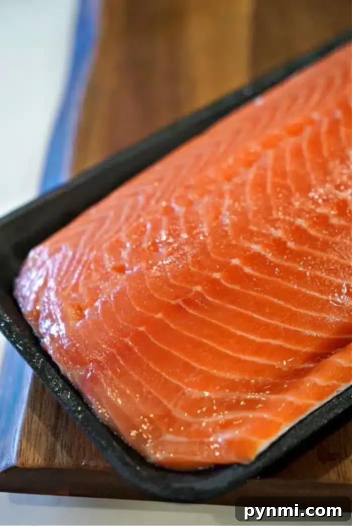 A beautifully seasoned raw salmon fillet generously coated with a rich, brown dry rub, ready for baking to achieve a fork-tender, flaky texture. This image highlights the preparation stage for the best baked salmon.
