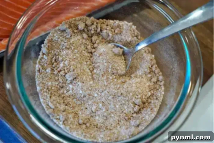A glass bowl holds a vibrant, rustic dry seasoning mix, with a spoon ready for application. In the background, a pristine raw salmon fillet awaits its transformation into the best baked salmon dish.