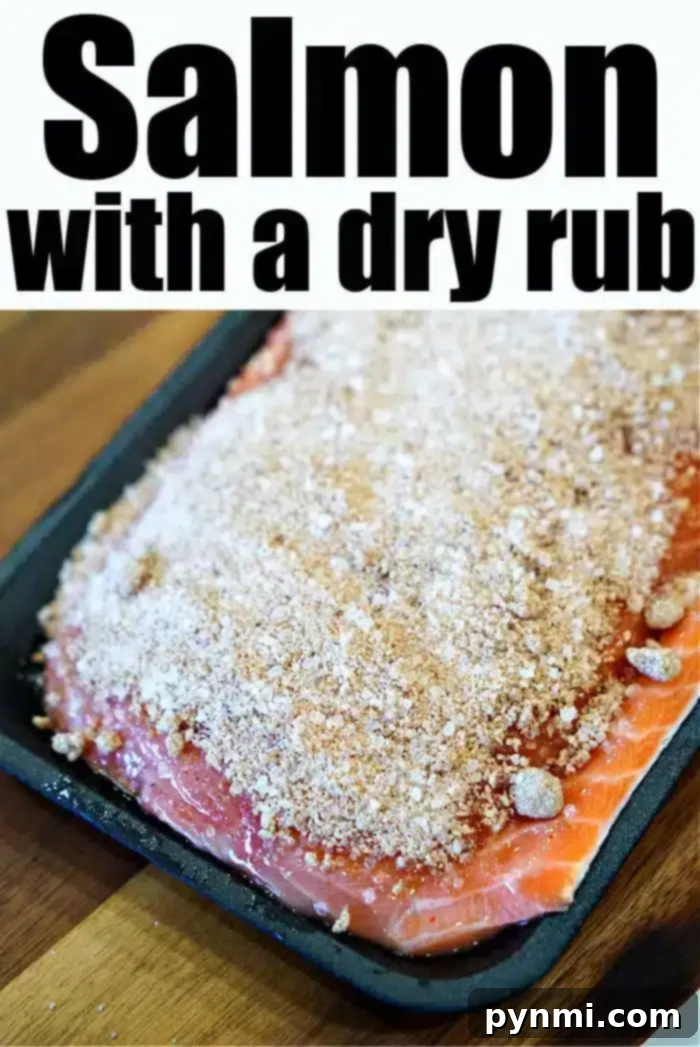 A raw salmon fillet, perfectly prepped and covered with a generous dry rub seasoning, rests on a black baking tray, ready for the oven. This image showcases the initial step towards the best baked salmon.