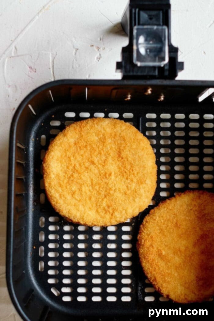 Two frozen chicken patties in an air fryer basket cooking to a crispy golden brown on a light-colored surface, demonstrating the perfect single-layer arrangement.