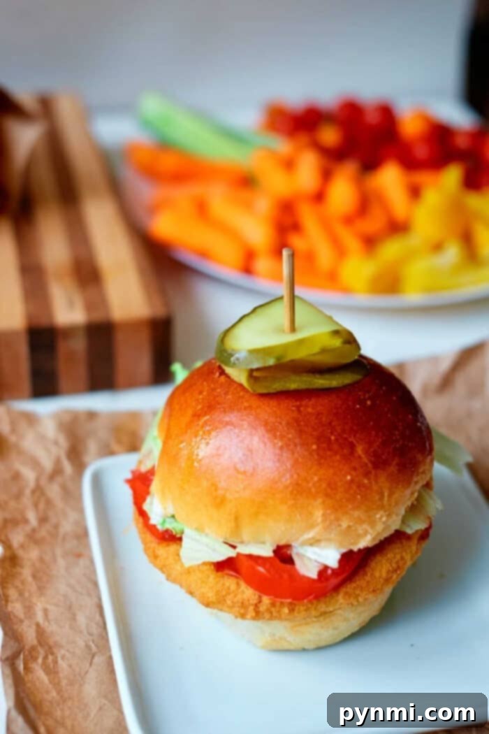 A perfectly prepared chicken sandwich made with a crispy frozen chicken patty cooked in an air fryer, artfully topped with fresh lettuce, a slice of ripe tomato, and crunchy pickles, served elegantly on a white plate with a side of golden fries.