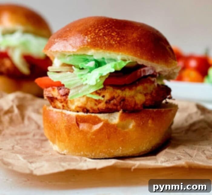 A perfectly cooked turkey burger with fresh lettuce and tomato on a toasted bun, ready to eat, next to an air fryer cooking another frozen turkey burger.