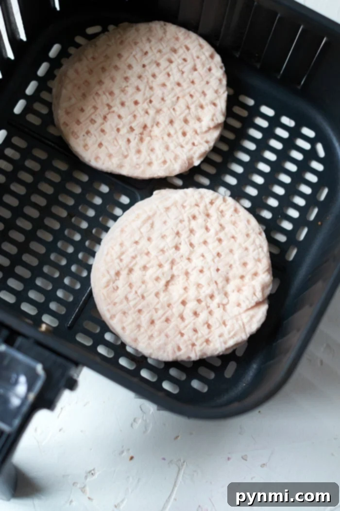 Two uncooked frozen turkey burger patties resting in an air fryer basket, ready for cooking.