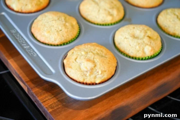Mayonnaise Magic Banana Bread 10 A tray of freshly baked banana bread muffins, made with a surprising hint of mayonnaise, rests in a metal muffin tin on a wooden surface.