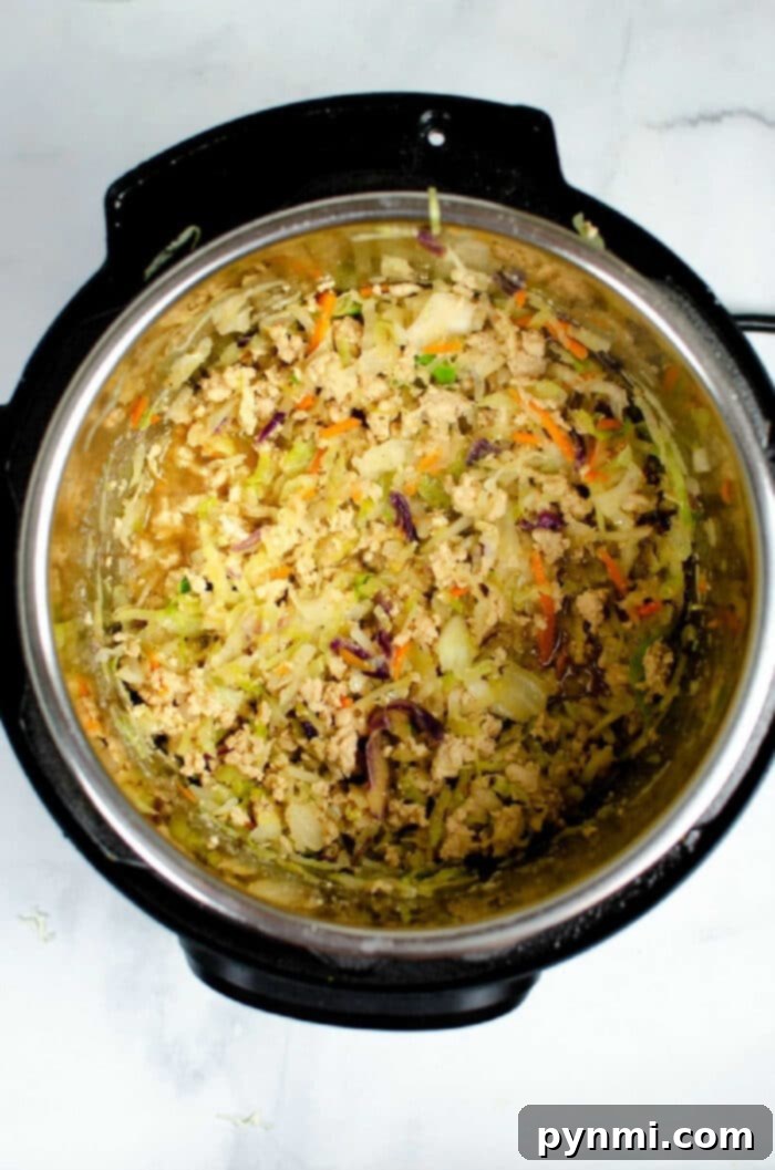 Speedy Instant Pot Egg Roll Bowls 4 Shredded vegetables and ground meat mixture for Instant Pot Egg Roll in a Bowl inside an Instant Pot, freshly cooked and fluffed, on a white surface.