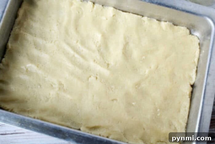 Unbaked sheet pan pumpkin pie dough evenly pressed into a rectangular metal baking pan on a light-colored surface.