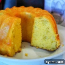 A close-up of a sliced cornbread bundt on a white plate reveals its golden-brown exterior and light, fluffy interior, reminiscent of air fryer cornbread. A bottle with a honey label is partially visible in the background.
