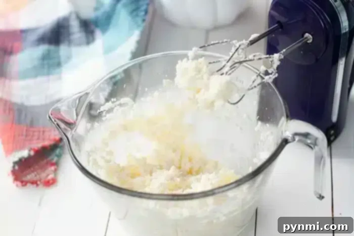 Effortless Half Sheet Cake Perfection 5 A clear glass mixing bowl containing a creamy mixture is placed on a white surface. An electric hand mixer with beaters covered in the mixture rests in the bowl, ready to whip up a 1/2 sheet cake.