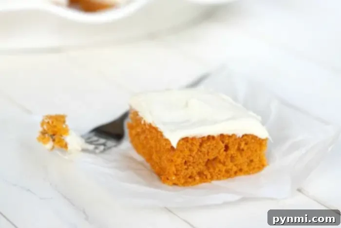 Effortless Half Sheet Cake Perfection 6 A slice of pumpkin cake with white frosting on top sits on a piece of parchment paper.
