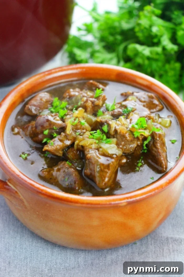 A bowl of beef stew meat garnished with parsley, showcasing perfectly tender beef tips with fresh herbs in the background.