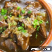 A close-up of a hearty bowl of beef stew garnished with chopped green herbs in a rustic brown ceramic bowl offers a glimpse into how to cook beef tips to perfection.
