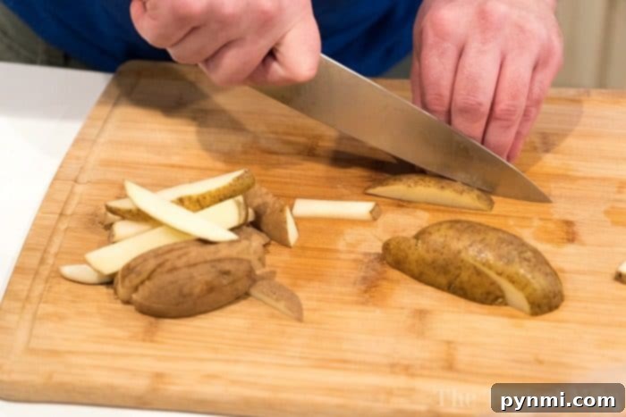A person expertly slicing potatoes into sticks on a wooden cutting board, preparing for delicious homemade french fries.