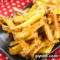 A pile of the best homemade french fries on a black plate, set on a red and white polka dot cloth.