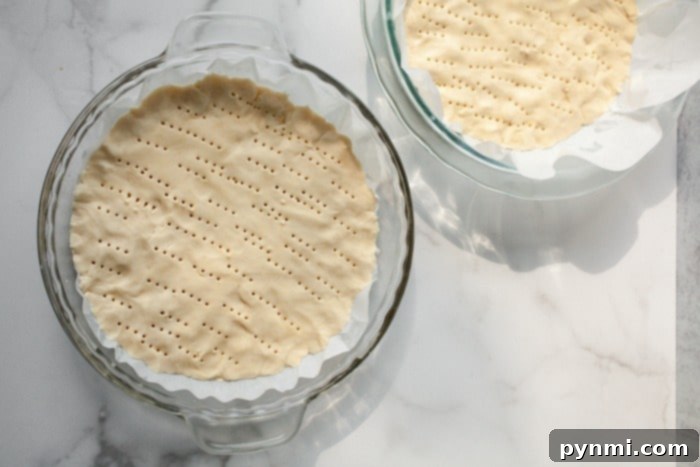Two pie dishes on a marble surface, with fork marks on the cookie dough, evoke the charm of baking Christmas tree sugar cookies during the festive season.