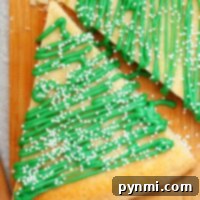 Triangle-shaped Christmas tree sugar cookies with green icing and white sprinkles rest elegantly on a wooden board.