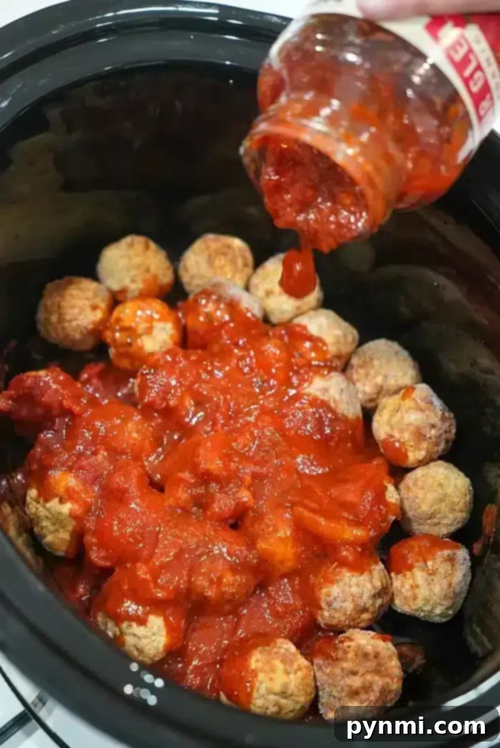 Frozen meatballs in the crockpot are being covered with tomato sauce poured from a jar.