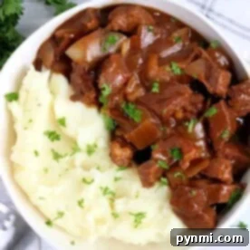 A savory bowl of mashed potatoes topped with beef stew and garnished with parsley, ready to be enjoyed.