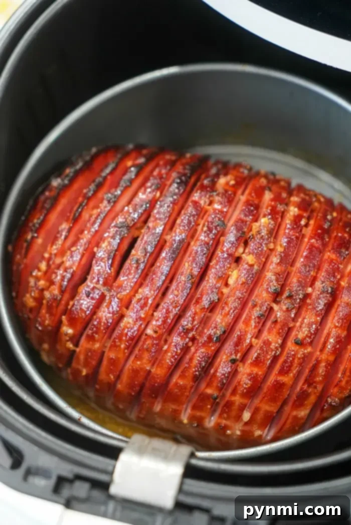 A honey-glazed boneless ham, beautifully scored and caramelized, rests in the black air fryer basket after cooking.