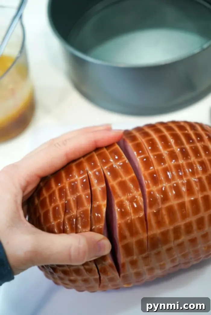 A hand skillfully slices a perfectly cooked air fryer ham, revealing its juicy interior and crispy, grid-patterned surface.